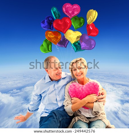 Happy mature couple with heart pillow against mountain peak through the clouds