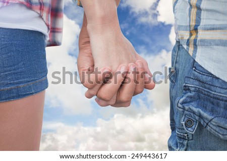 Couple in check shirts and denim holding hands against blue sky with white clouds