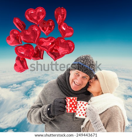 Happy mature couple in winter clothes holding mugs against blue sky over white clouds