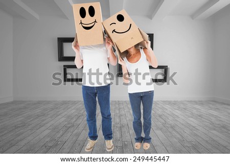 Mature couple wearing boxes over their heads against big room with several frames at wall