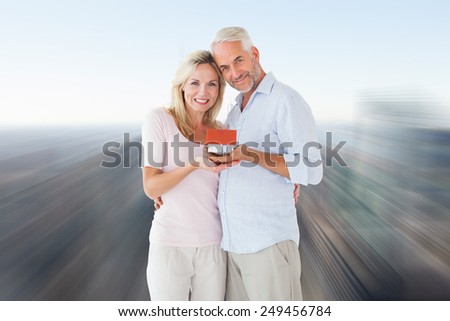 Happy couple holding miniature model house against city skyline