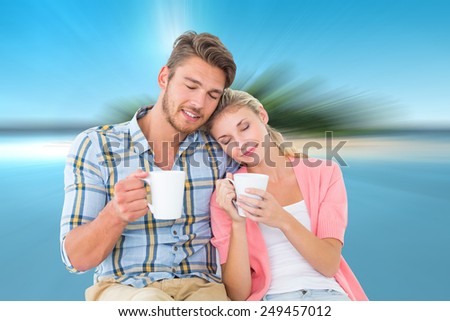 Attractive young couple sitting holding mugs against tropical island in blue ocean