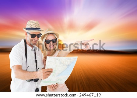 Happy tourist couple using map and pointing against countryside scene