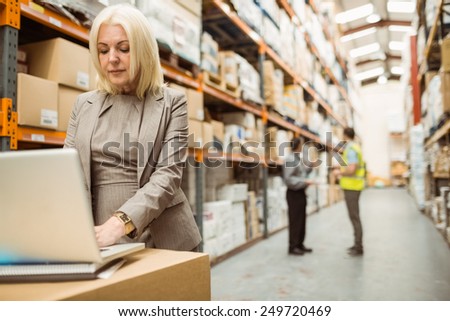 Focused warehouse manager working on laptop in a large warehouse