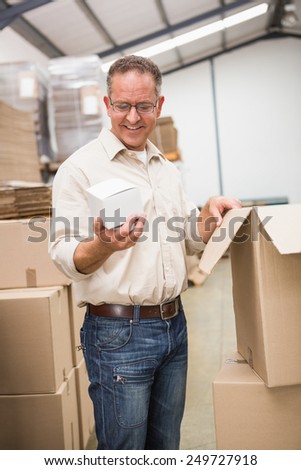 Smiling warehouse worker holding small box in a large warehouse