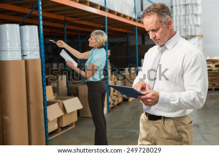 Smiling warehouse manager using tablet pc in a large warehouse