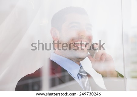 Smiling businessman looking out window on the phone in his office