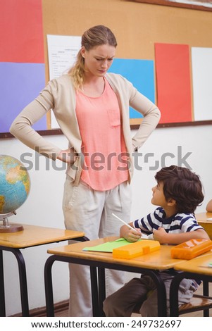 Angry teacher looking pupil with hands on hips at the elementary school