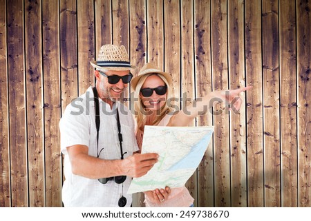 Happy tourist couple using map and pointing against wooden planks background