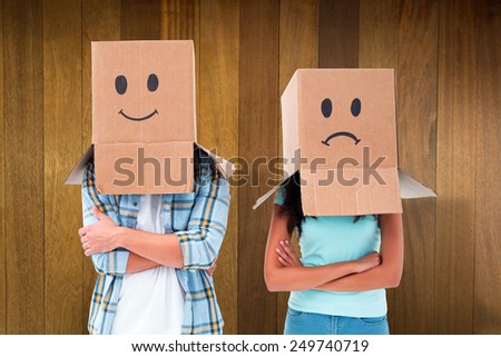Young couple wearing sad face boxes over head against wooden surface with planks