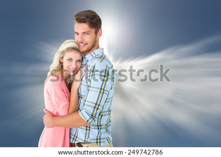 Attractive couple embracing and smiling at camera against blue sky with clouds and sun