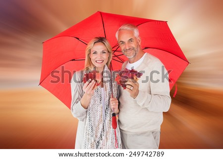 Smiling couple showing autumn leaves under umbrella against sunrise over field with tree
