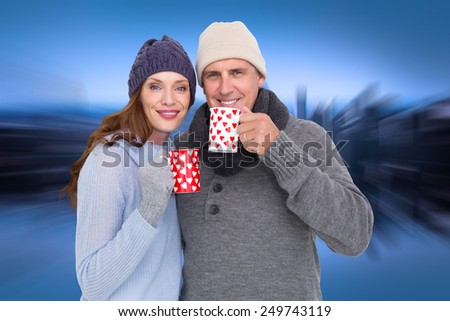Happy couple in warm clothing holding mugs against mirror image of city skyline