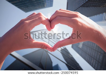 Hands making heart shape on the beach against skyscraper