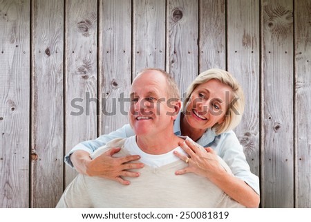 Happy mature man giving piggy back to partner against wooden planks