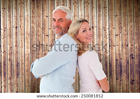 Smiling couple standing leaning backs together against wooden planks