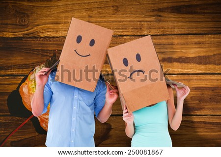 Couple wearing sad face boxes on their heads against wooden table with autumn leaves