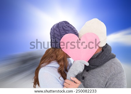 Couple in warm clothing holding heart against large rock overlooking bright sky