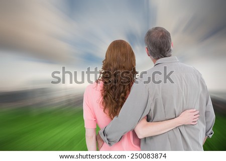 Casual couple standing arm around against cloudy sky over city