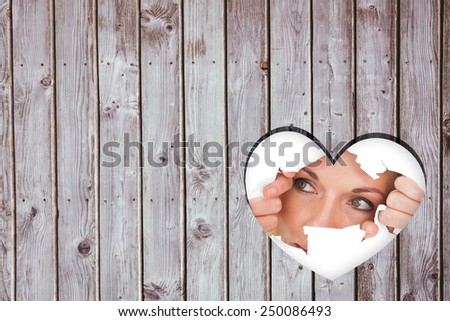 Woman looking through torn paper against heart in wood