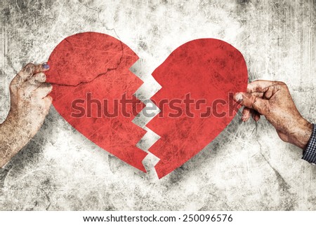 Two hands holding broken heart against grey background