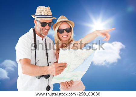 Happy tourist couple using map and pointing against bright blue sky with clouds