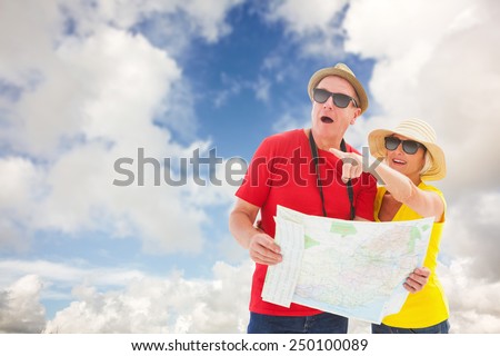 Happy tourist couple using map against blue sky with white clouds