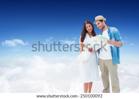Happy hipster couple looking at map against bright blue sky over clouds