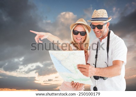 Happy tourist couple using map and pointing against blue and orange sky with clouds