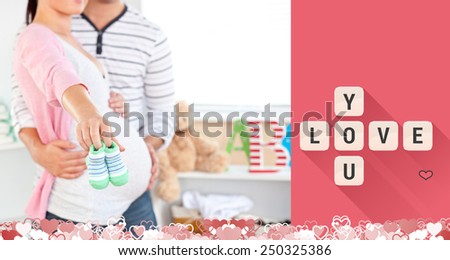 Close up of a bright pregnant woman holding baby shoes while husband touching her belly in the room against love you tiles