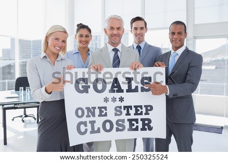 Business team holding large blank poster and pointing to it against goals one step closer