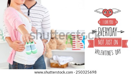 Close up of a bright pregnant woman holding baby shoes while husband touching her belly in the room against cute valentines message