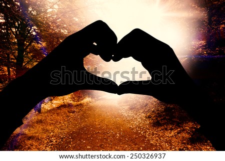 Woman making heart shape with hands against forest trail