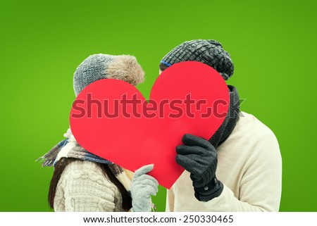 Attractive young couple in warm clothes holding red heart against green vignette