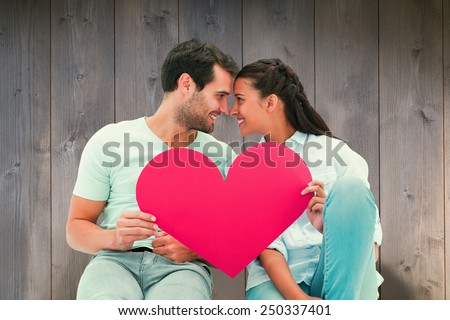 Cute couple sitting holding red heart against wooden planks