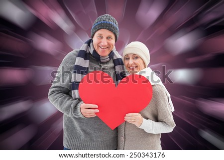 Happy mature couple in winter clothes holding red heart against valentines heart pattern