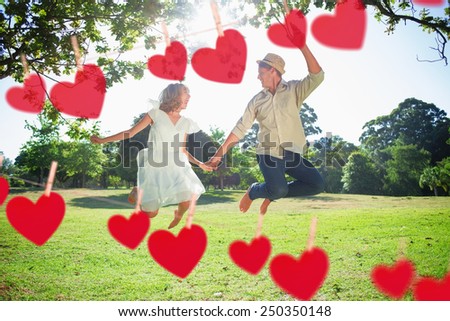 Cute couple jumping in the park together holding hands against hearts hanging on a line