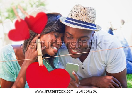 Happy couple lying in garden together listening to music against hearts hanging on a line