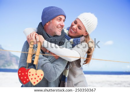 Attractive couple hugging on the beach in warm clothing against hearts hanging on the line