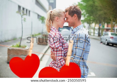 Couple in check shirts and denim hugging each other against hearts hanging on a line