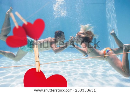 Cute couple kissing underwater in the swimming pool against hearts hanging on a line