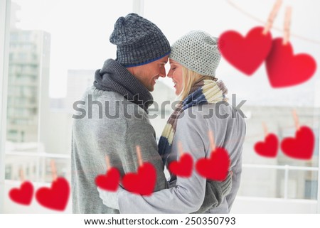 Cute couple in warm clothing hugging against hearts hanging on a line