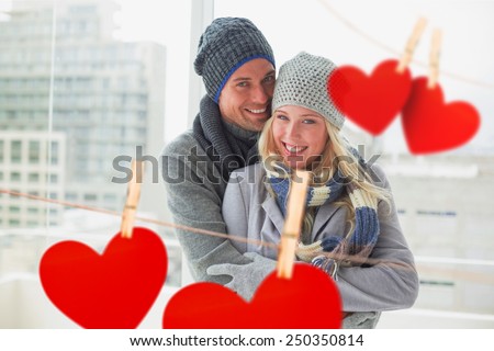 Cute couple in warm clothing smiling at camera against hearts hanging on a line