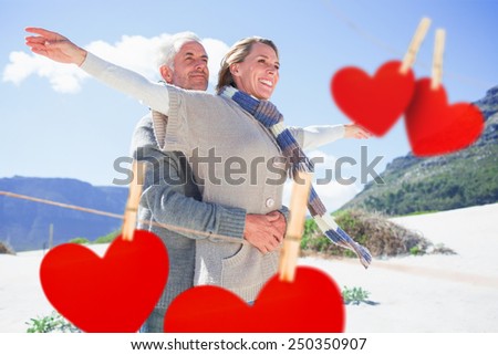 Carefree couple hugging on the beach in warm clothing against hearts hanging on a line