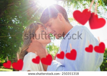 Cute couple hugging and smiling in the park against hearts hanging on a line