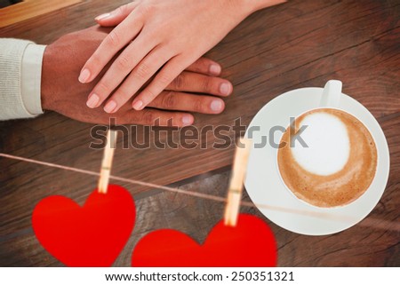 Couple holding hands beside cappuccino against hearts hanging on a line