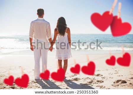 Attractive couple holding hands and watching the waves against hearts hanging on a line
