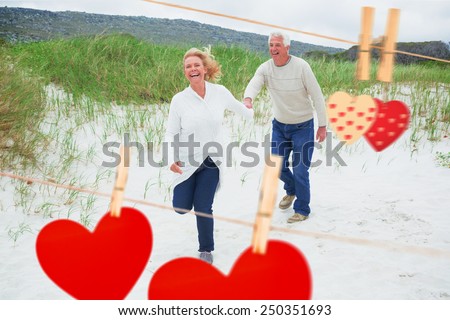 Cheerful senior couple running at beach against hearts hanging on the line