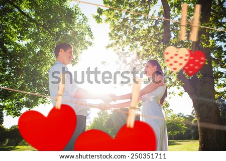 Loving young couple holding hands at park against hearts hanging on the line