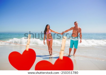 Smiling handsome man holding his girlfriends hand against hearts hanging on a line